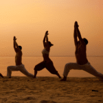 Three people on a beach at sunrise doing yoga.