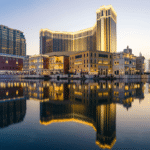 A large hotel with its reflection on water. Hotel is gold in color.